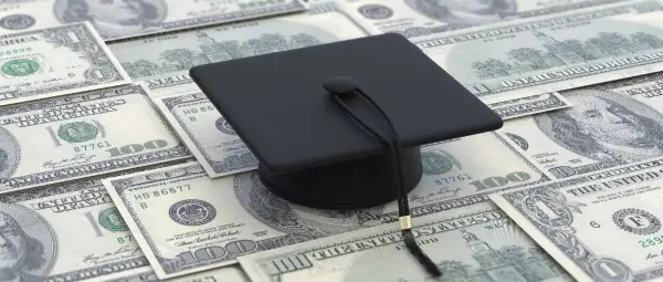 Black graduation cap sitting on one hundred dollar bills
